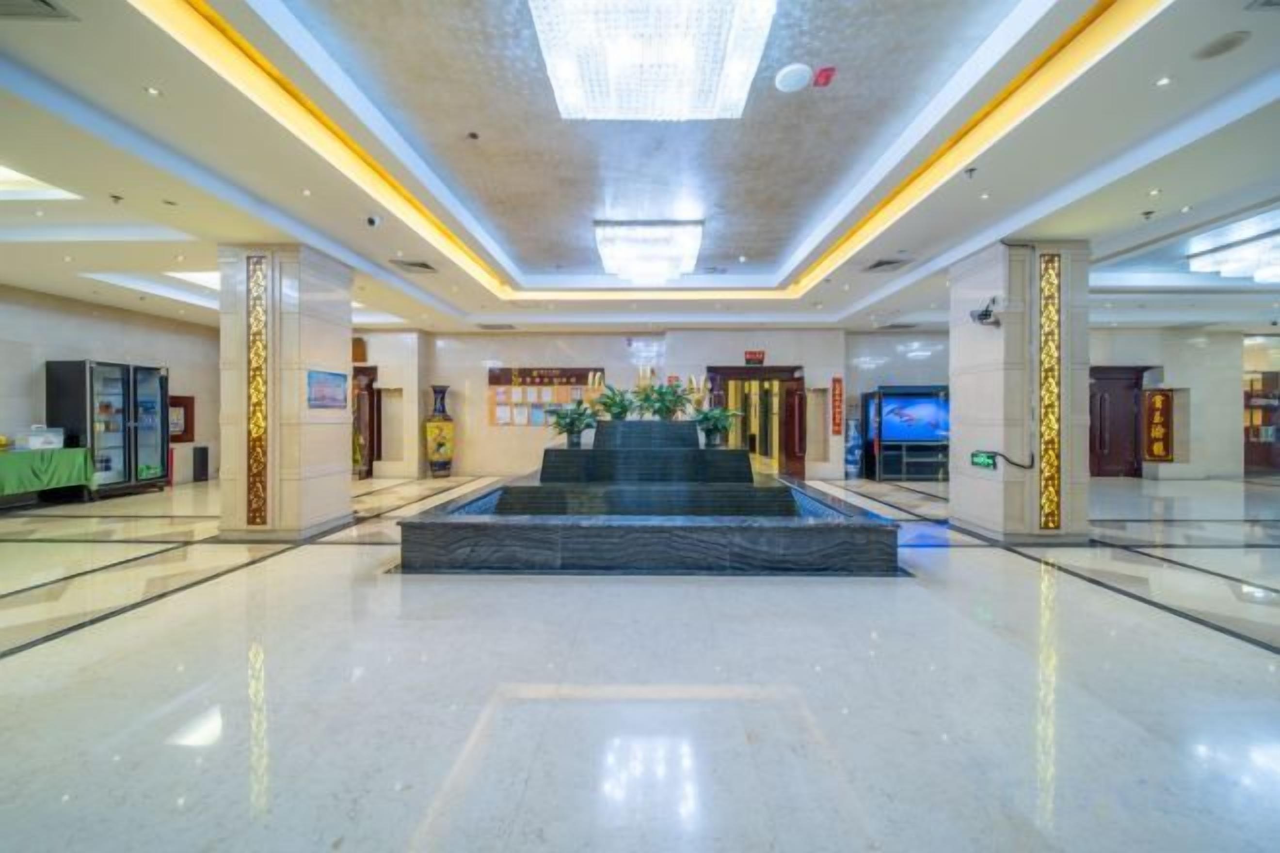 A spacious lobby with a central water feature, a reception desk, and a large digital screen.