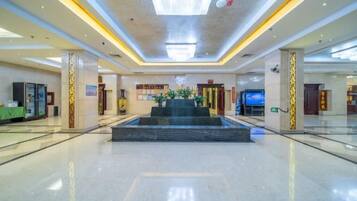 A spacious lobby with a central water feature, a reception desk, and a large digital screen.