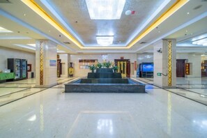 A spacious lobby with a central water feature, a reception desk, and a large digital screen. - Yulong Hotel (Wusu)
