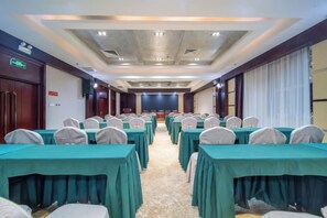A conference room with rows of tables and chairs, a stage at the front, and a carpeted floor. - Yulong Hotel (Wusu)