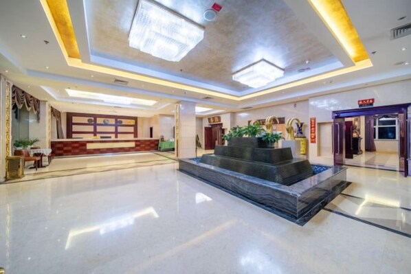 A spacious lobby with a reception desk, a seating area, and a water feature. - Yulong Hotel (Wusu)