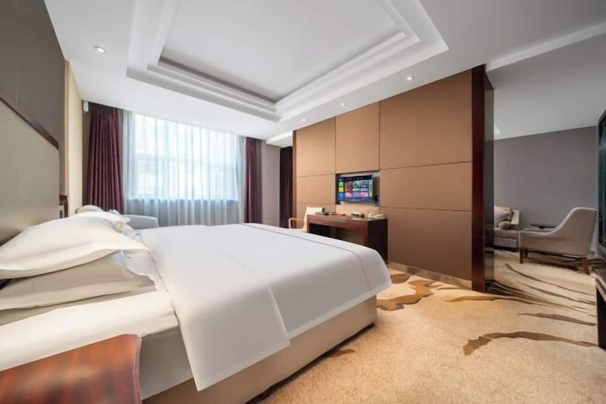 A modern hotel room with a large bed, a desk, a TV, and a chair.