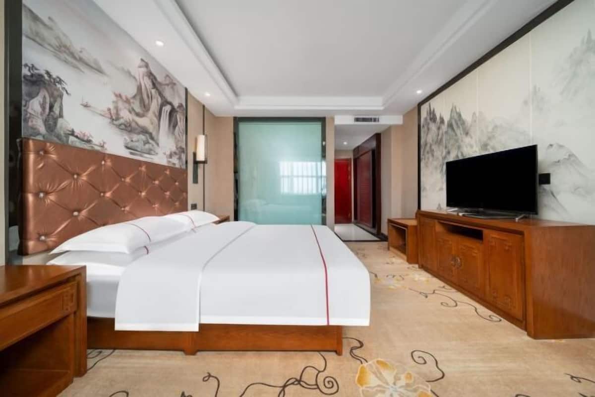 A hotel room with a large bed, a television, a wooden cabinet, and a mural on the wall.