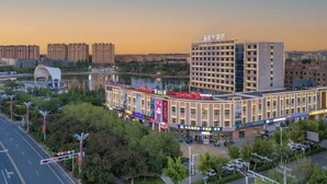 A multi-story hotel with a modern facade, located near a body of water with a bridge and greenery. - Yulong Hotel (Wusu)