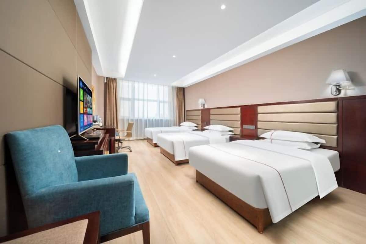 A hotel room with a large bed, a desk with a computer, a blue armchair, and a TV on the wall.