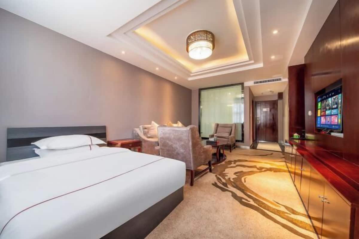 A hotel room with a large bed, a seating area with chairs, a television, and a carpeted floor.