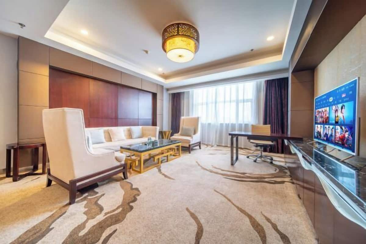 A hotel room with a sofa, armchairs, a coffee table, a TV, and a large window.