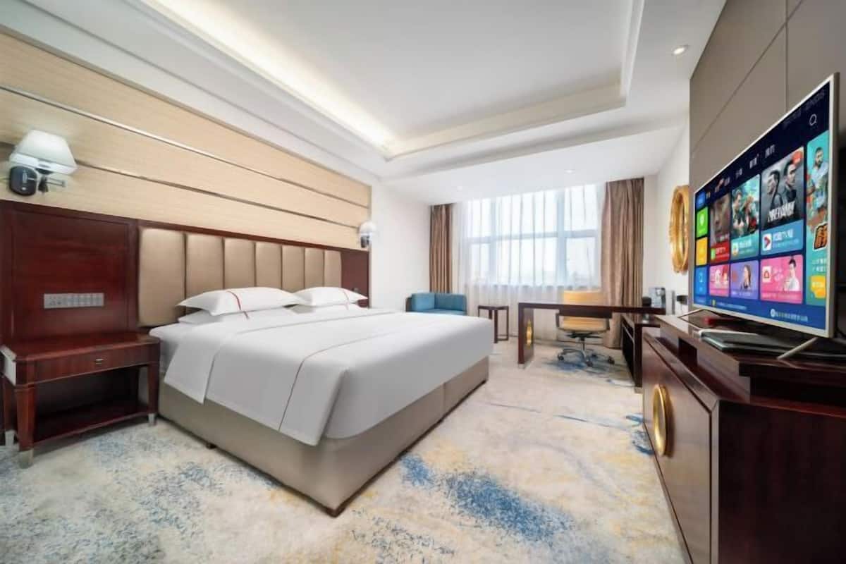 A hotel room with a large bed, a desk, a television, and a window with curtains.