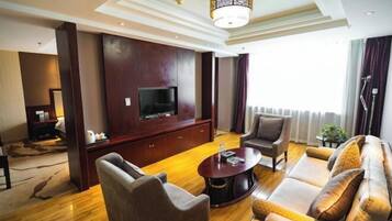 A modern living room with a flat-screen TV, leather sofas, a coffee table, and a large window with curtains.