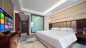 A hotel room with a large bed, a TV on a wooden stand, a desk with a lamp, and a sliding door leading to another room. - Yulong Hotel (Wusu)