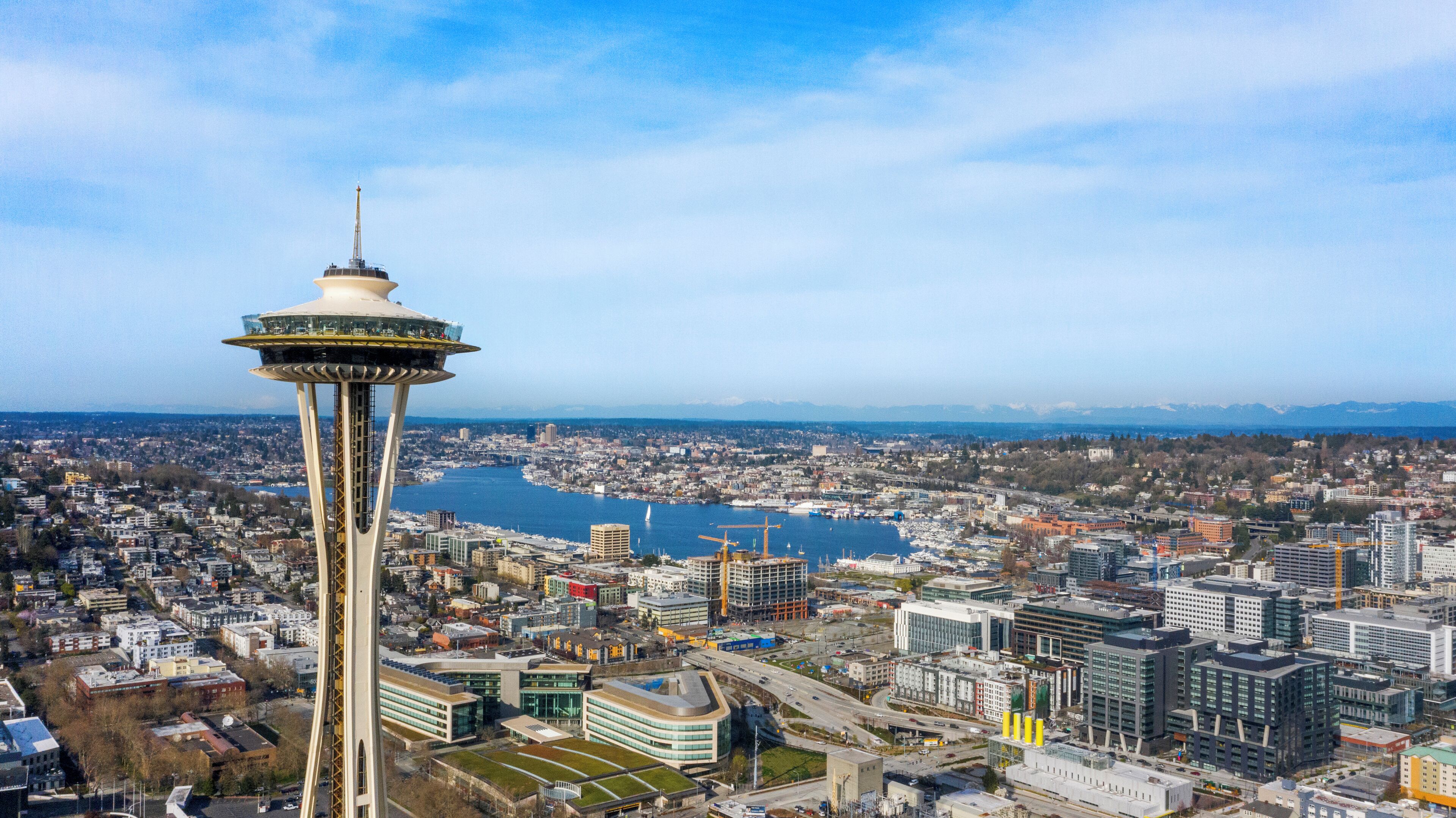 A high-rise tower with a viewing platform, surrounded by a cityscape with buildings and a body of water.