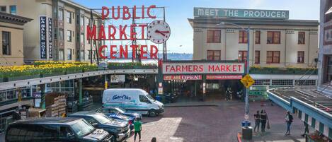 A public market center with a clock, a Farmers Market sign, and a 'Meet the Producer' sign.
