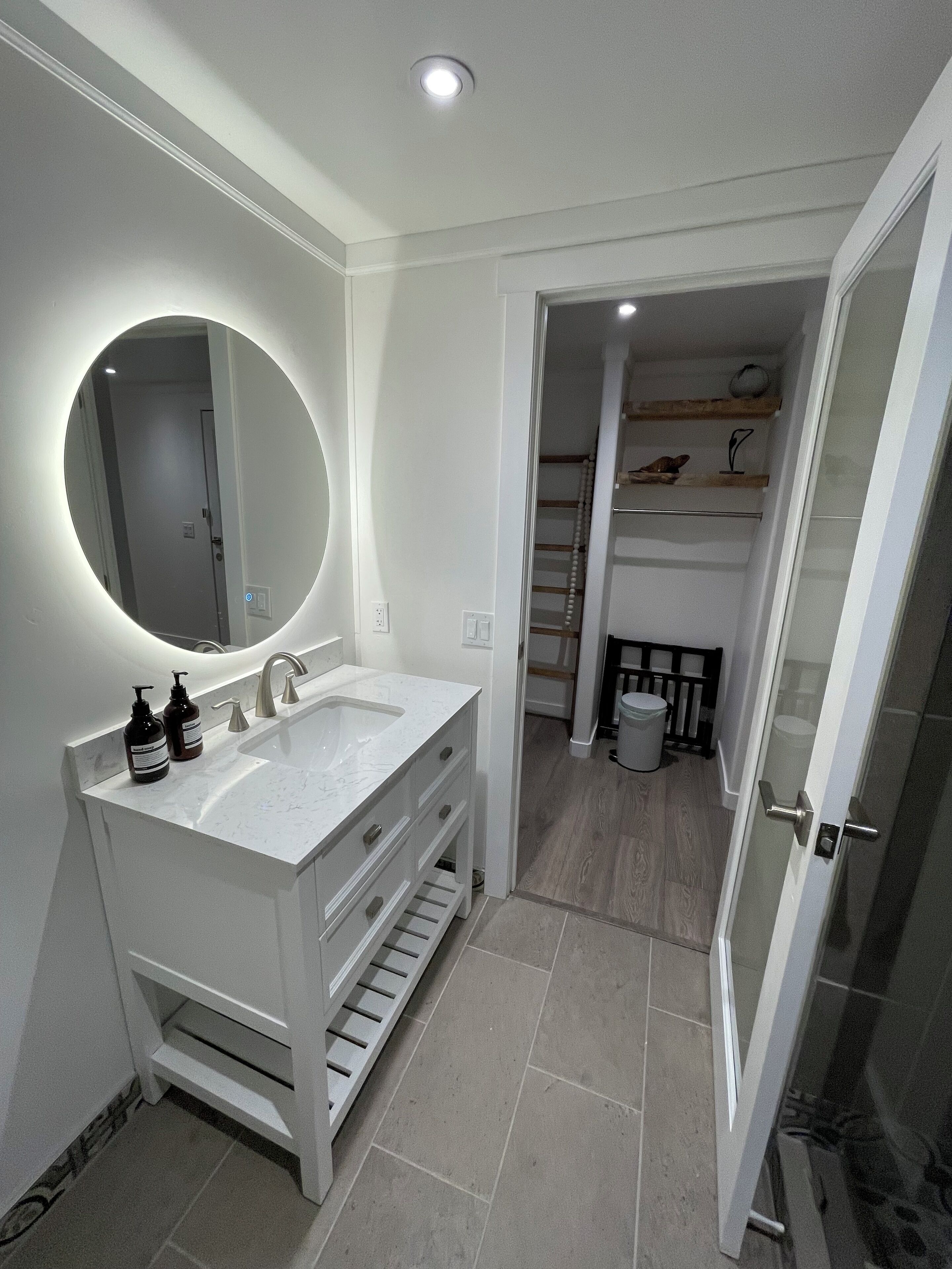 Une salle de bain moderne avec un meuble-lavabo blanc, un grand miroir et une douche à l’italienne.