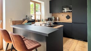 A modern kitchen with a central island, black cabinets, and a window providing natural light.