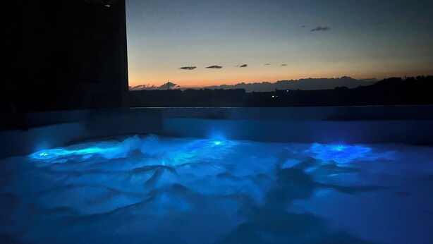 A hot tub with blue lighting, a view of the sky, and a distant mountain range.