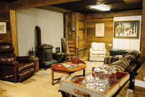 A cozy room with a leather armchair, a wooden sofa, a plaid-patterned table, and a vintage stove.