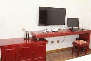 Una stanza con una TV montata a parete, una scrivania con un computer, un armadietto rosso e uno sgabello.