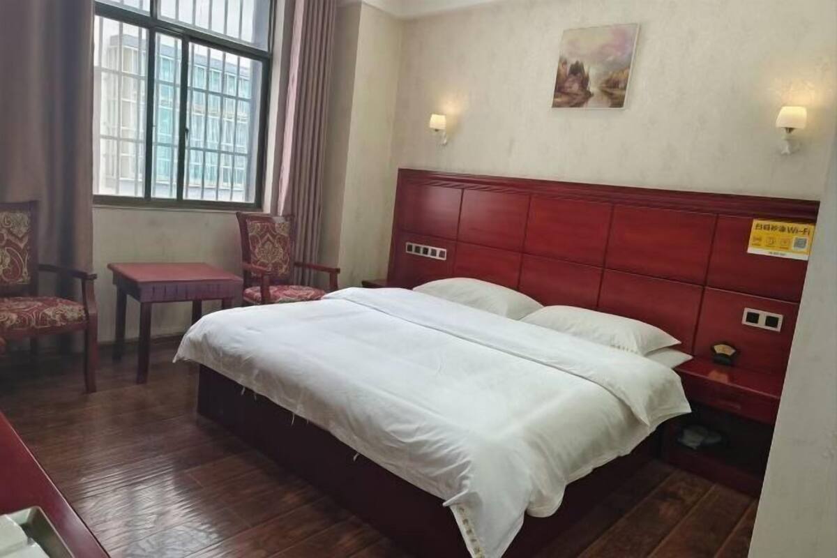 Una habitación de hotel con cama, una silla, una mesita de noche, una lámpara y una ventana.