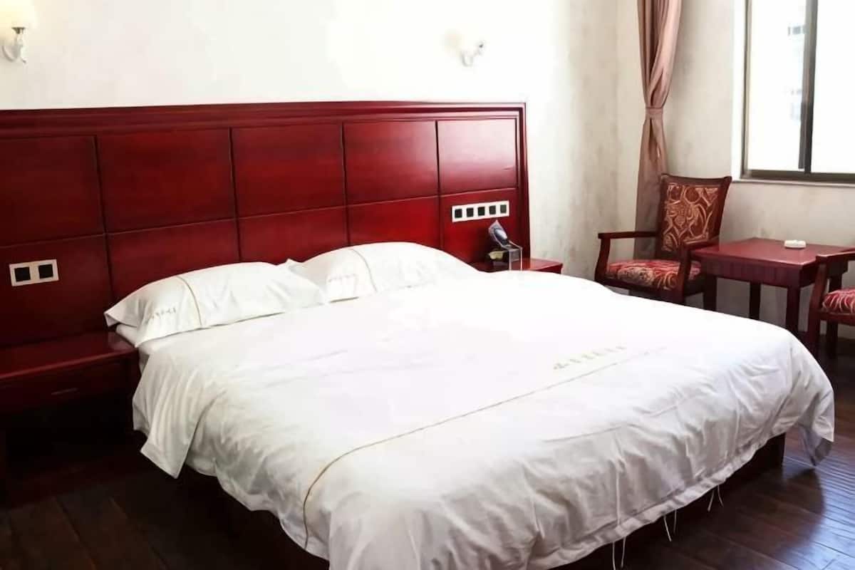 Una cama bien hecha con sábanas blancas, un cabecero de madera, una mesita de noche, una silla y un escritorio con silla.