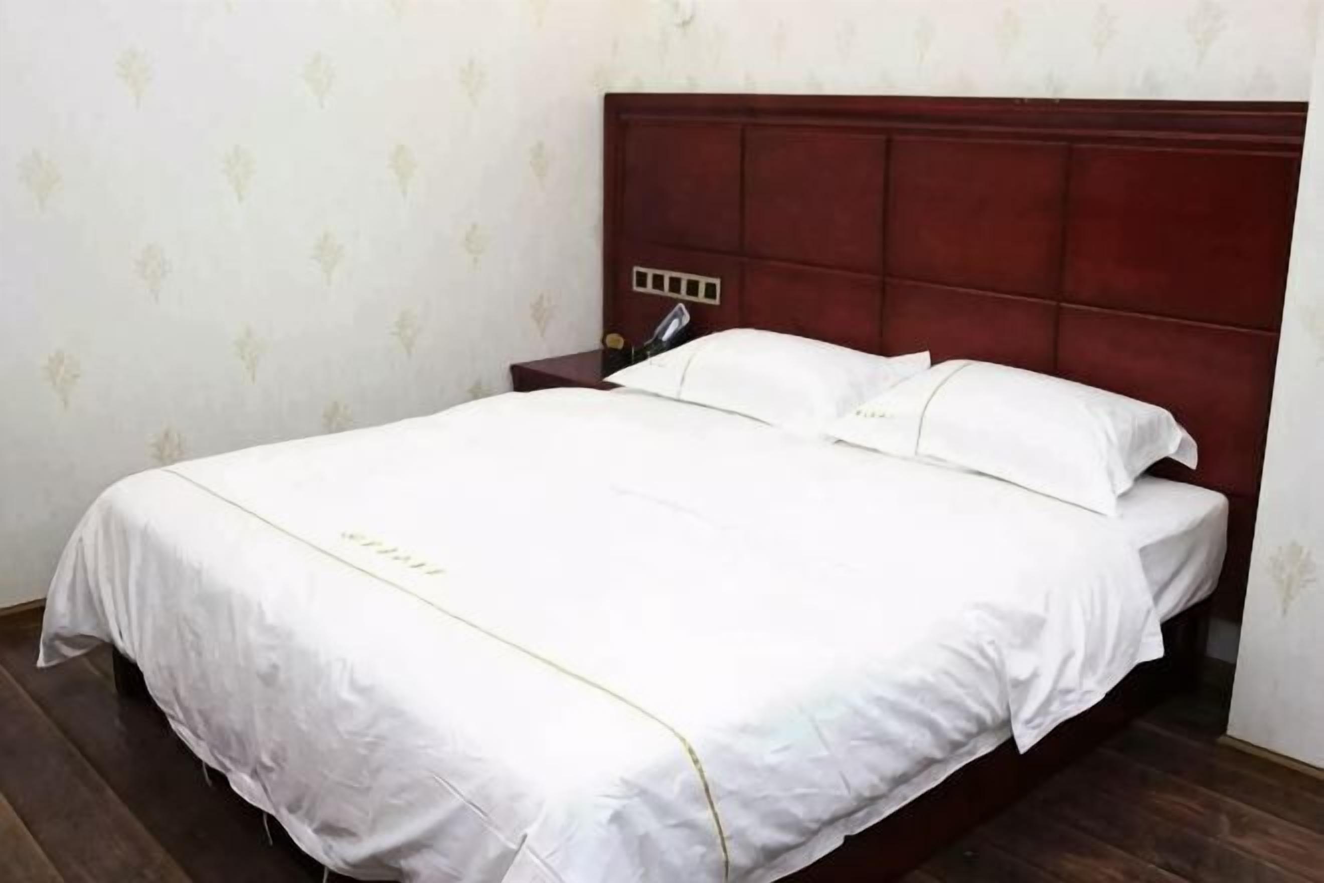 Un letto rifatto con cura, una testiera in legno, un comodino con una lampada e una parete con una decorazione discreta.