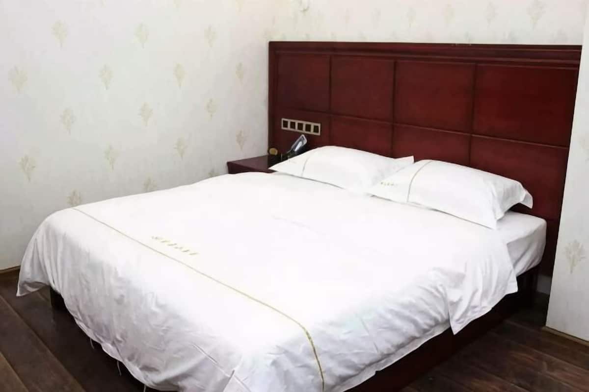 Una cama bien hecha con cabecera de madera, una mesita de noche con lámpara y una pared con un discreto estampado.