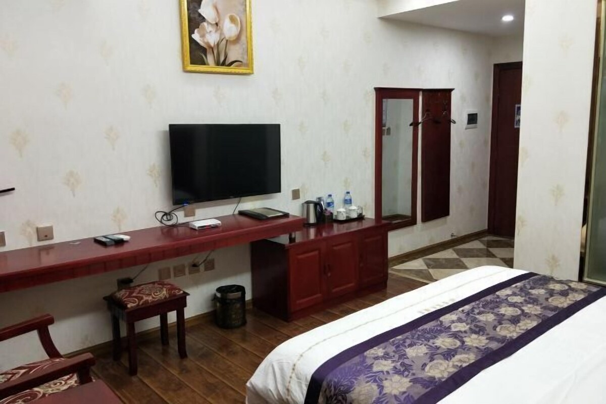 Una habitación de hotel con cama, escritorio con televisor, espejo y armario.