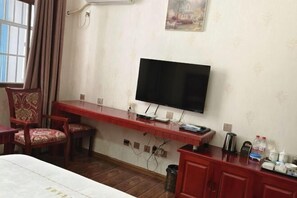 Una habitación con una cama, un escritorio con televisión de pantalla plana, una silla y una mesita con hervidor y tazas.