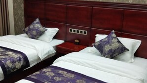 Habitación de hotel con dos camas, cada una con colcha y almohadas estampadas con motivos florales. La cabecera es de madera oscura y hay una mesita de noche roja entre las camas.