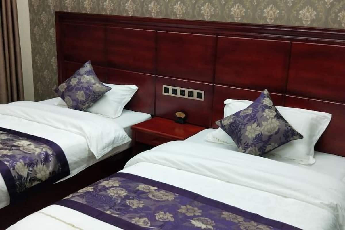 Habitación de hotel con dos camas, cada una con colcha y almohadas estampadas con motivos florales. La cabecera es de madera oscura y hay una mesita de noche roja entre las camas.