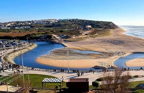 A coastal area with a beach, a curved water body, and a road leading to a parking area.