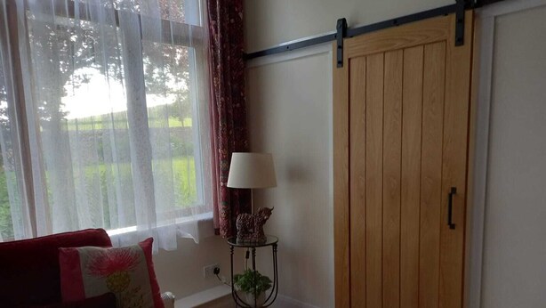 Ein gemütliches Wohnzimmer mit einem roten Sofa, einem kleinen Beistelltisch mit einer Lampe und einer Holztür.