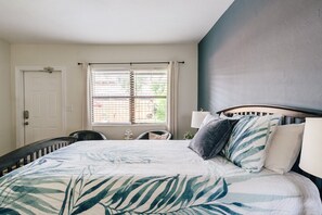 A bedroom with a bed, a window with blinds, a door, and a chair.