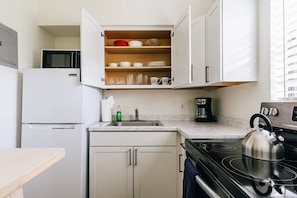 A compact kitchen with a microwave, stove, and a shelf with dishes and glasses.