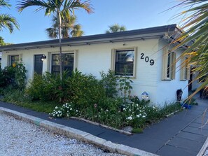 A single-story building with the number 209, surrounded by lush greenery and flowers.