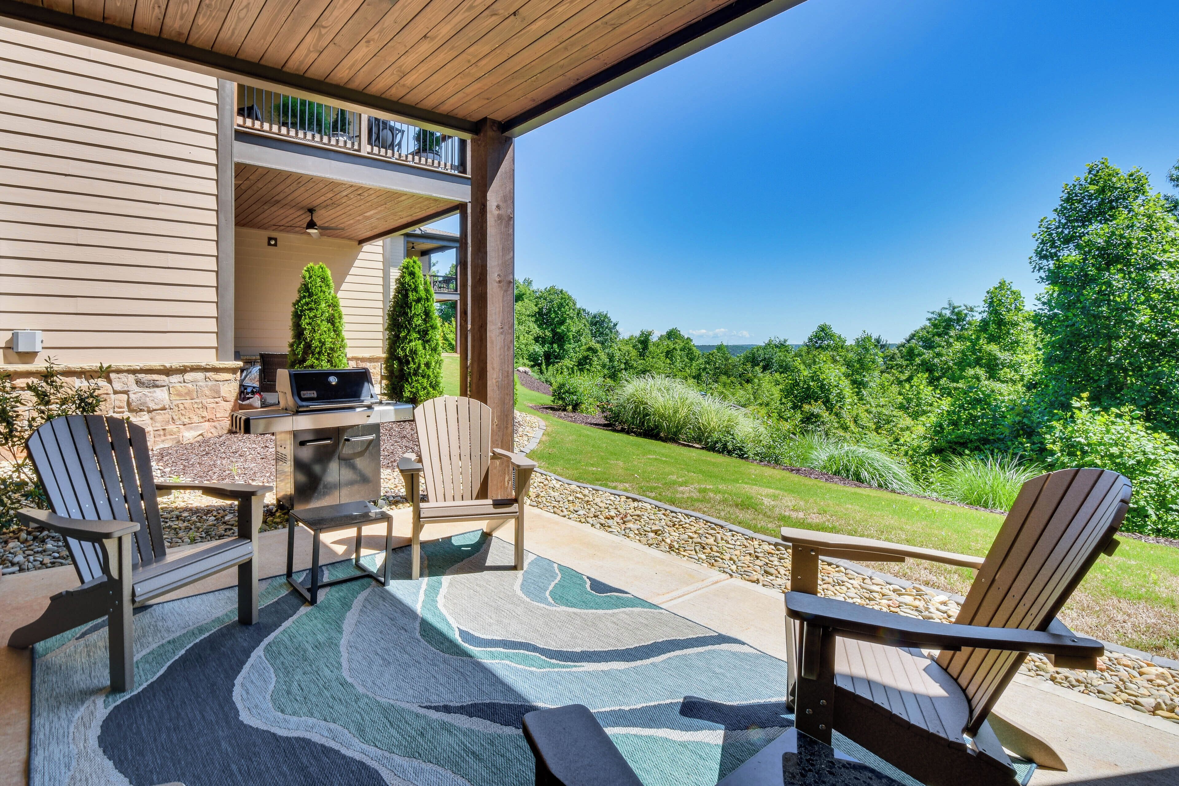A covered patio with Adirondack chairs, a grill, and a view of a lush green landscape.