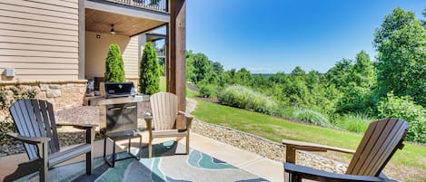 A covered patio with Adirondack chairs, a grill, and a view of a lush green landscape.