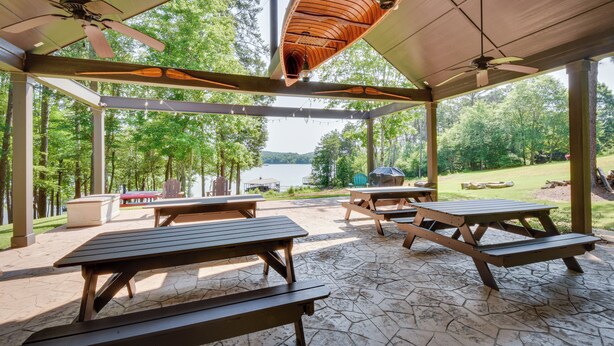 En udendørs pavillon med picnicborde, ventilator og udsigt over en sø.