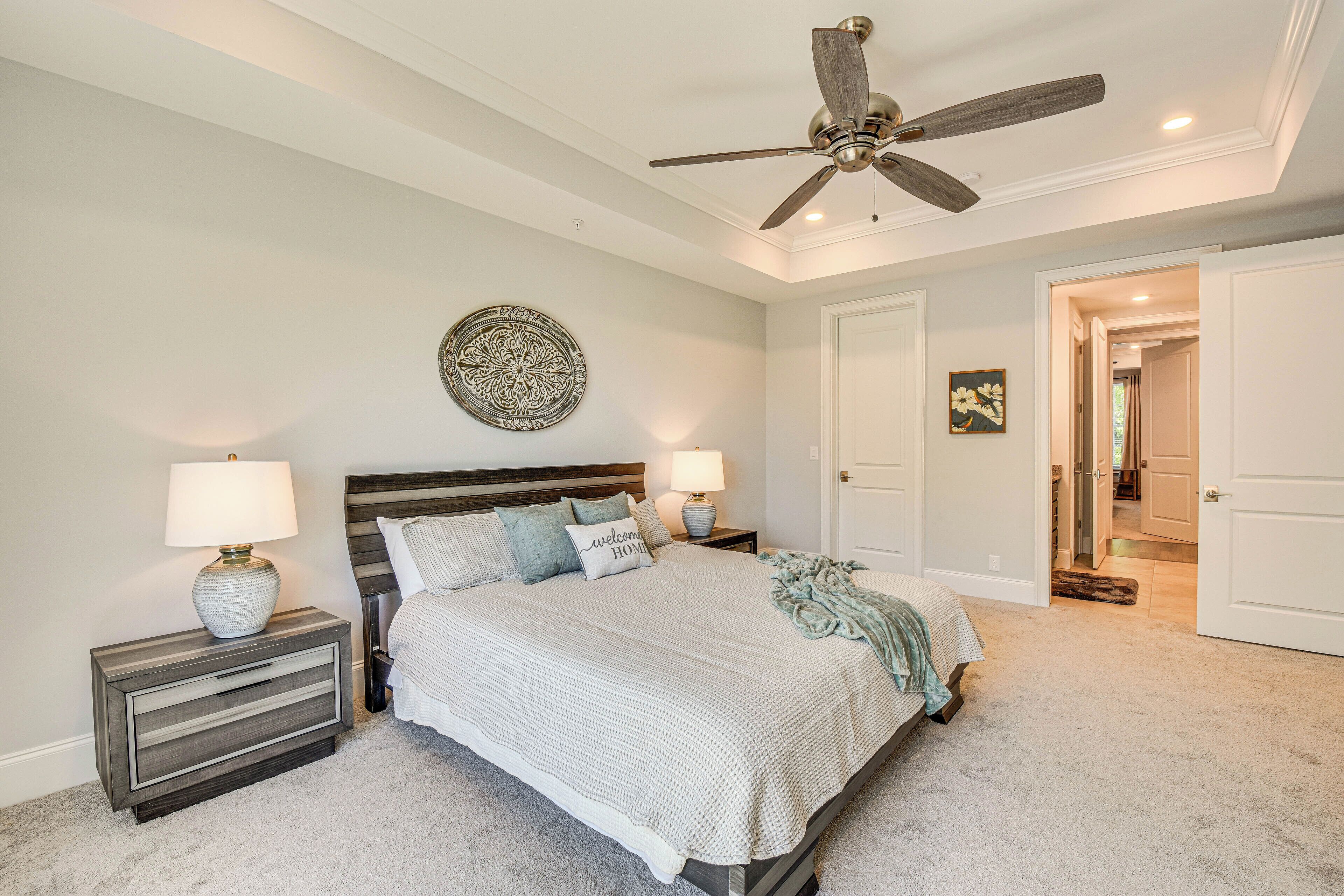 A bedroom with a bed, nightstands, a ceiling fan, and a door leading to another room.