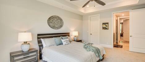 A bedroom with a bed, nightstands, a ceiling fan, and a door leading to another room.