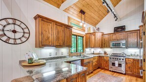 A kitchen with wooden cabinets, granite countertops, a stainless steel stove, and a large clock on the wall. - Group-Friendly Golf Getaway! 5 Mi to Cashiers (Cullowhee)