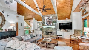 A spacious living room with a stone fireplace, a ceiling fan, and a mounted deer head. - Group-Friendly Golf Getaway! 5 Mi to Cashiers (Cullowhee)