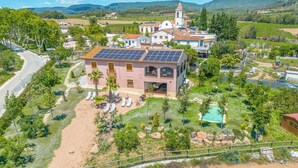 A pink villa with a solar panel roof, a swimming pool, and a church in the background. - Cozy home in Guardiola de Fontrubí with sauna (Guardiola de Fontrubí)