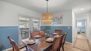 A dining area with a wooden table set for six, surrounded by chairs, a hanging light fixture, and a vase with flowers. - Reserve your stay today! Canal-front rental with a boat dock available. (Crystal River)