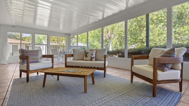 A spacious patio with a wooden table and two sofas, large windows offering a view of greenery. - Reserve your stay today! Canal-front rental with a boat dock available. (Crystal River)