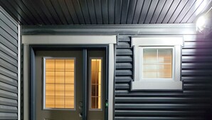 Une façade en bois sombre avec deux portes, une petite fenêtre et deux chaises rouges.