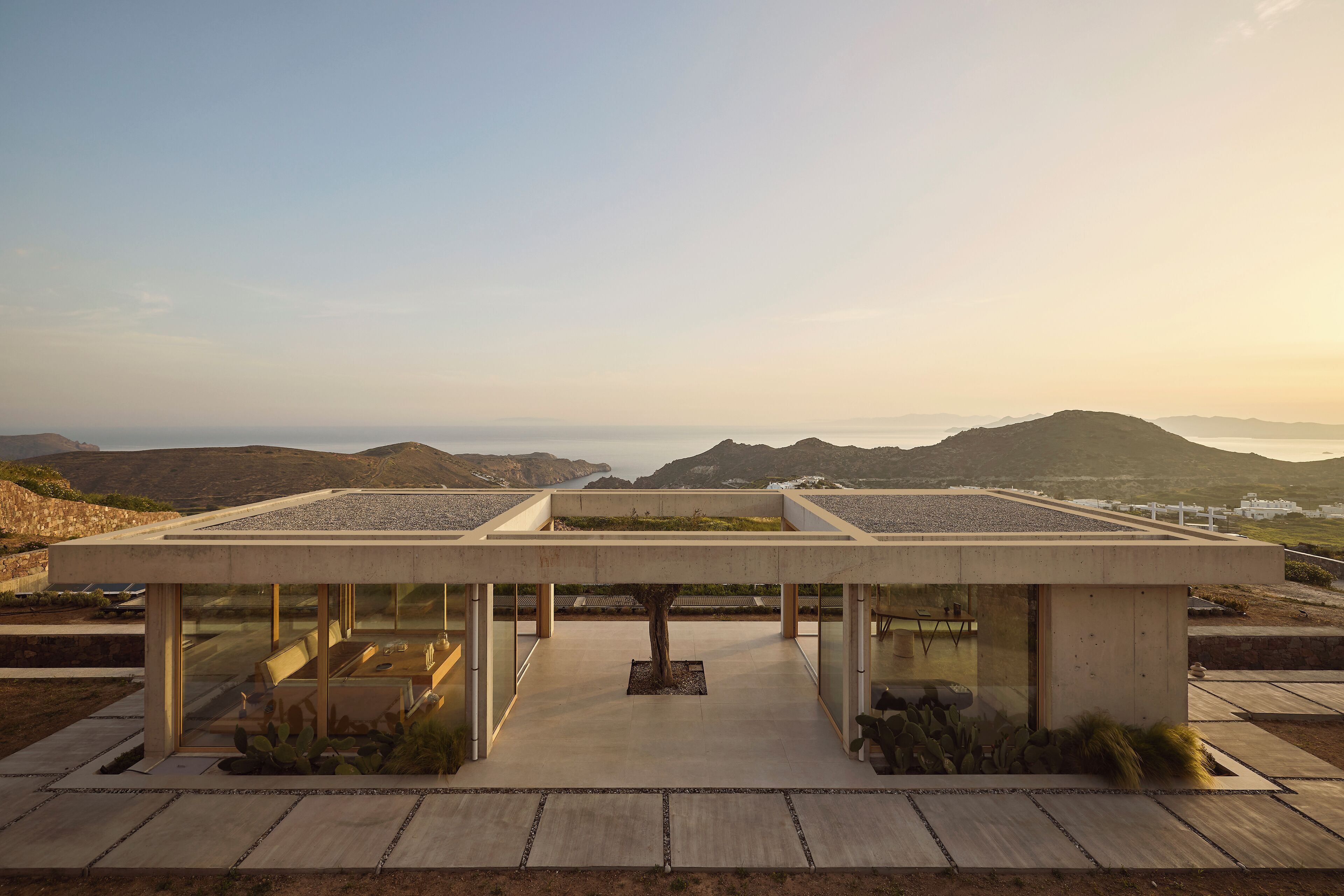 Un espace de détente extérieur moderne, doté d’une structure en béton, entouré d’une végétation désertique et offrant une vue sur un paysage montagneux.