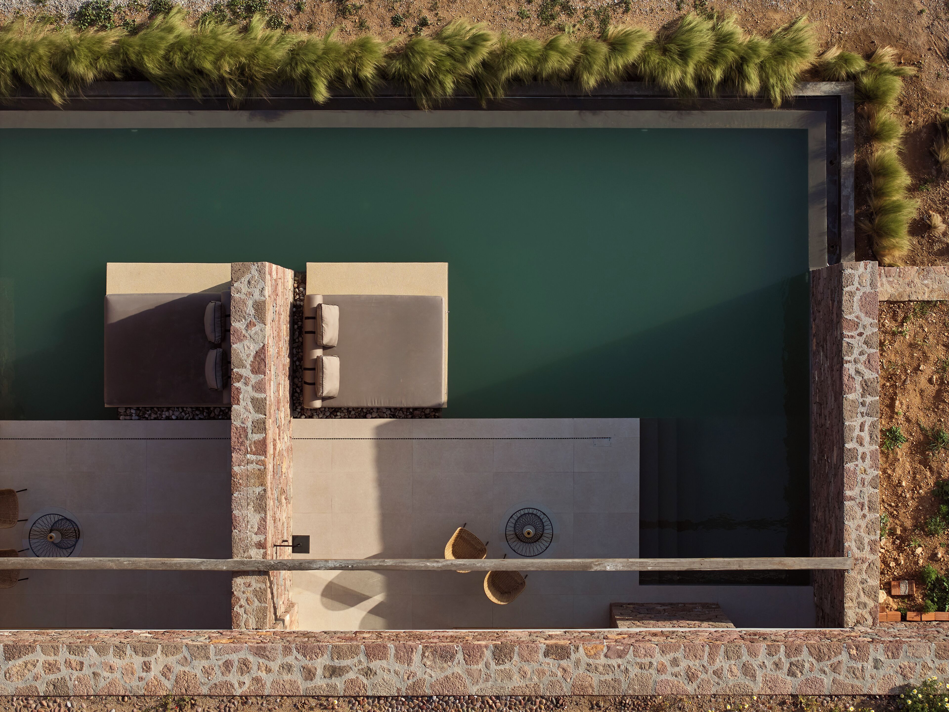 Un área de piscina en la azotea con una silla de descanso y una mesa, rodeada por un muro de piedra y vegetación.