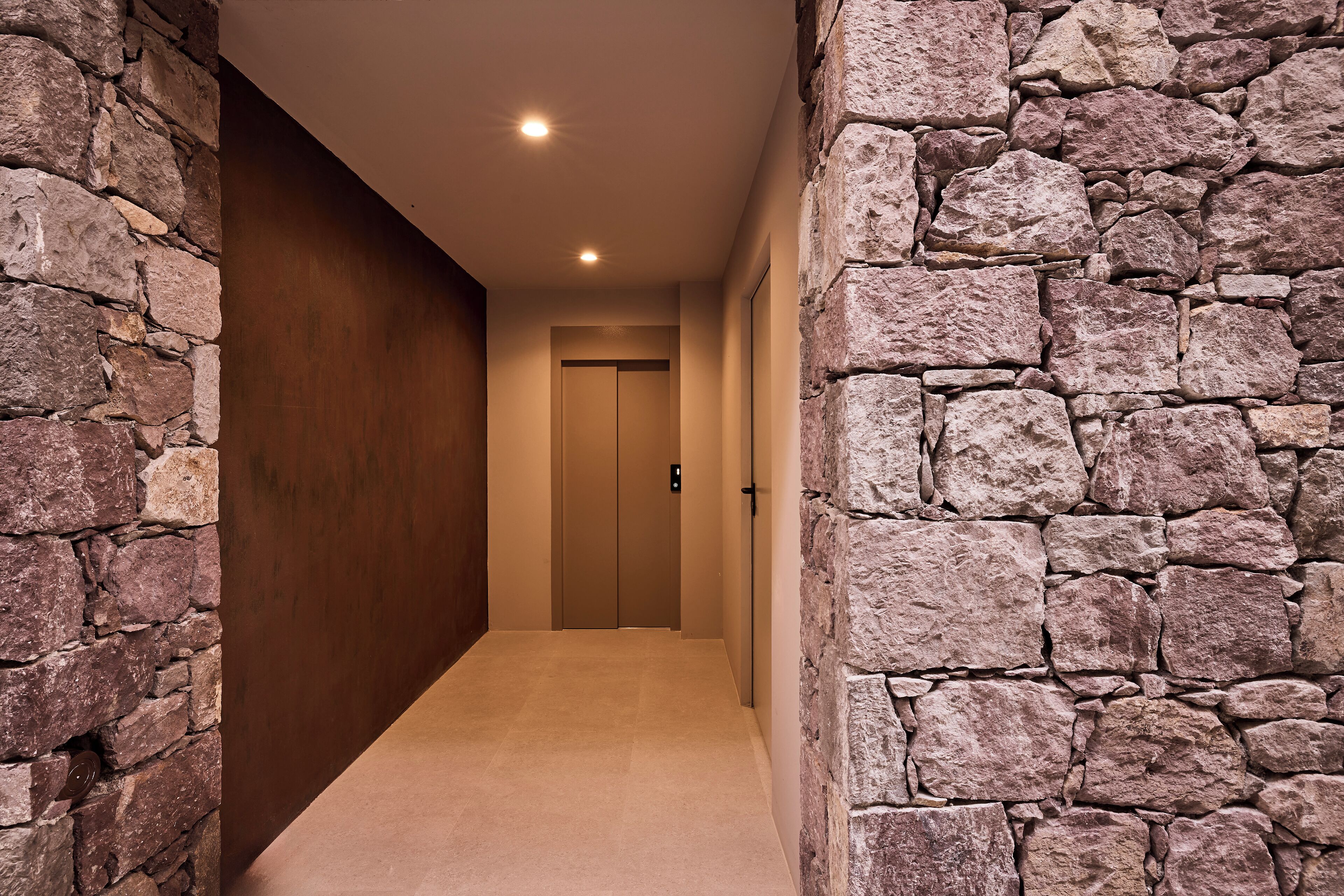 Un pasillo con paredes de piedra y suelo de madera, que conduce a una puerta al final.