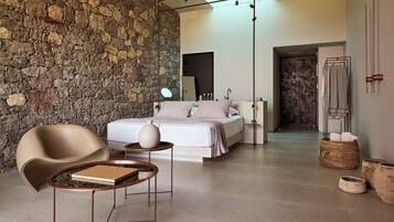 Un dormitorio moderno con pared de piedra, una cama con ropa blanca, una silla, una mesita de noche y una lámpara colgante.