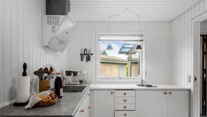 Uma cozinha com armários brancos, uma janela grande e bancada com diversos eletrodomésticos e utensílios.
